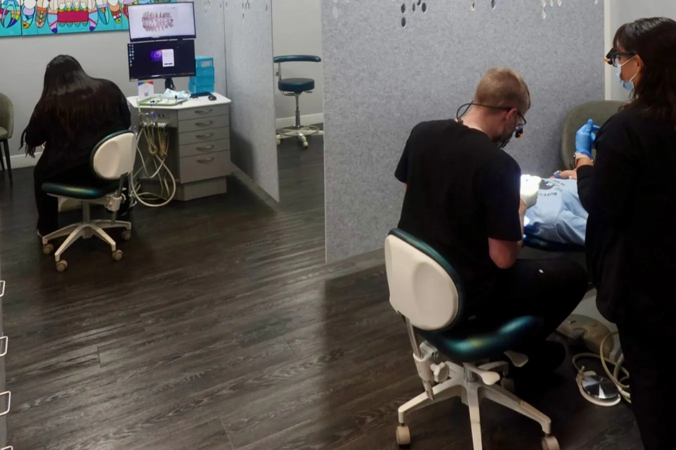 Dental professionals providing orthodontic treatment in a clinical setting, featuring a patient receiving care and a monitor displaying dental information.