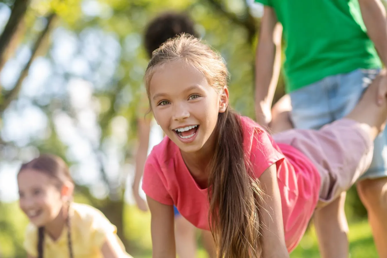 Smiling girl in a pink shirt playing with friends outdoors, highlighting the fun and confidence associated with Invisalign for kids.