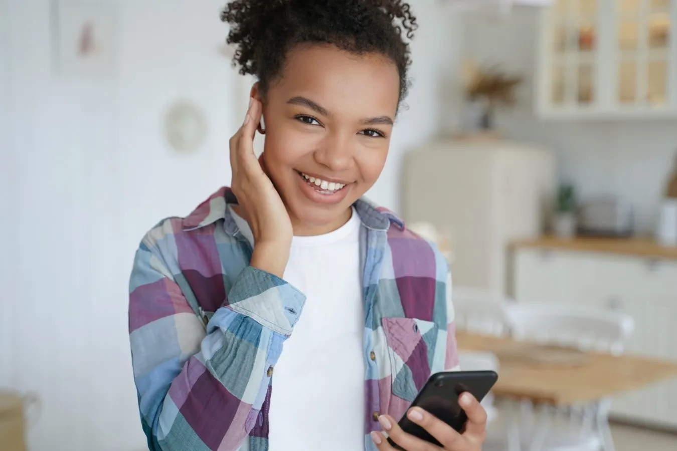 Smiling young girl in a plaid shirt holding a smartphone, illustrating the importance of communication and engagement in orthodontic care at Berger Orthodontics.