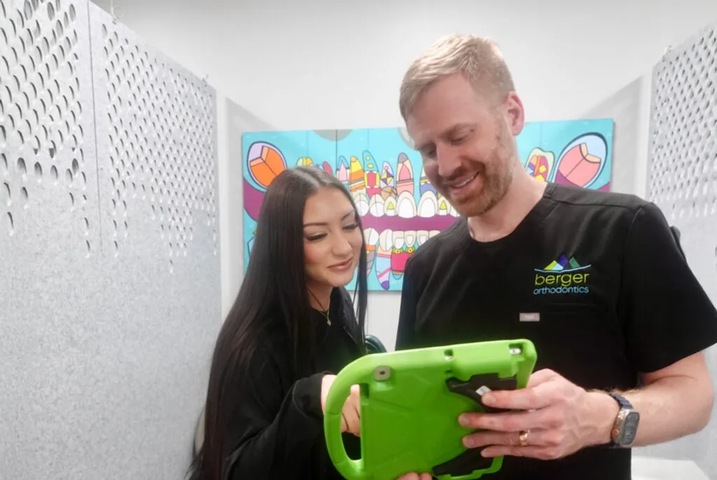 Patient and orthodontist reviewing dental information on a tablet in a colorful orthodontic office setting.